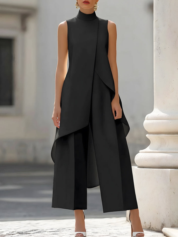Schwarzes Set mit ärmellosem asymmetrischem Oberteil und weiter Hose, frontal getragen vor einer weißen Säule. 2