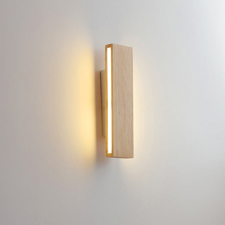 Schrägansicht der senkrechten Holzleuchte mit seitlich leuchtendem Lichtstreifen, der die Wand dahinter warm anstrahlt. 10