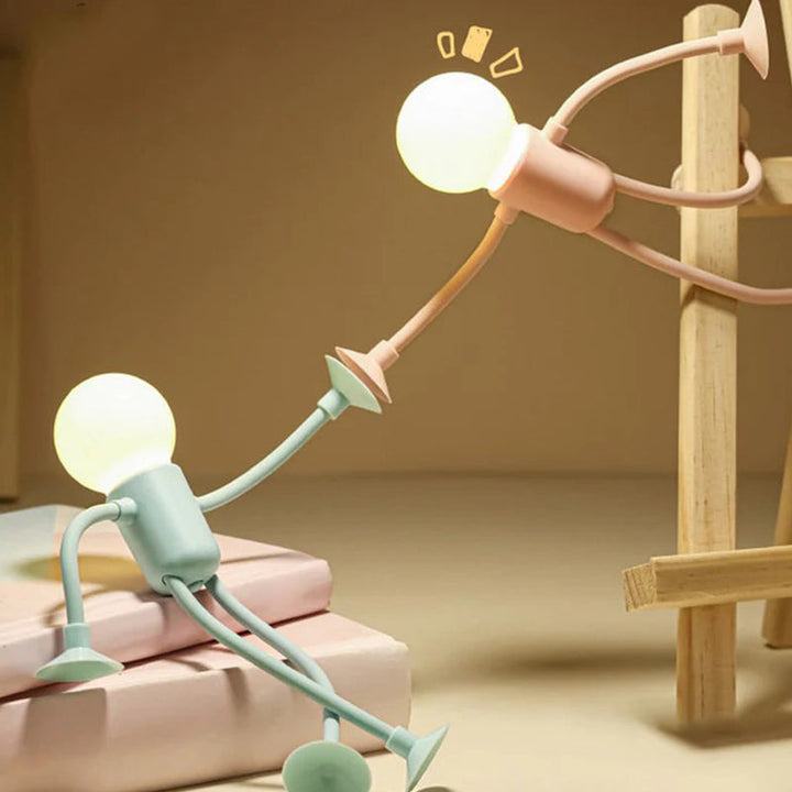 Mintgrüne Lampe sitzt auf rosa Büchern, eine rosa Lampe hängt mit gestrecktem Arm an einem Holzgestell und greift nach ihr. 6