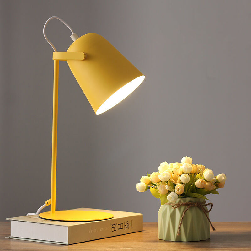 Gelbe Tischlampe mit eimerförmigem Schirm auf einem Buch, daneben eine Vase mit hellen Röschen auf einem Holztisch. 1