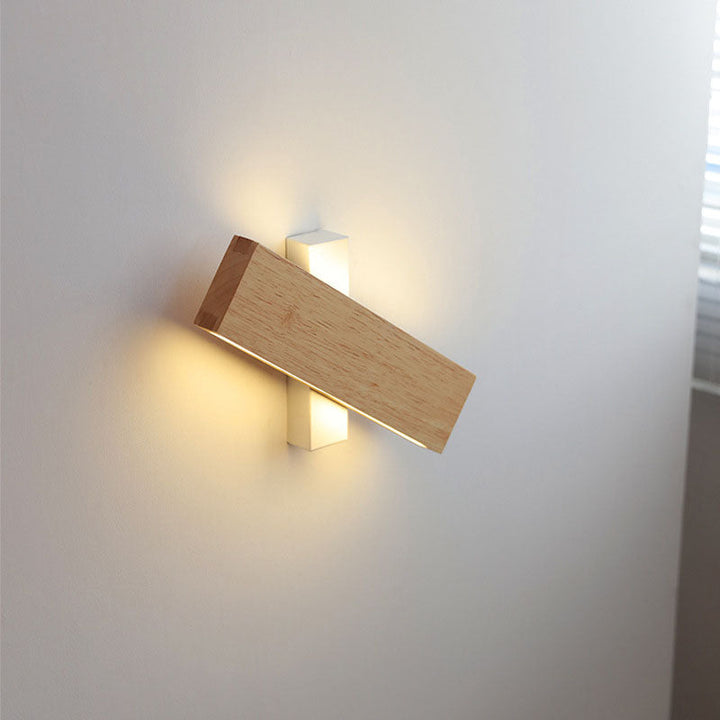 Querliegende Holzleiste kreuzförmig vor der weißen Halterung, warmes Licht oben und unten an einer Wand neben einem Fenster. 9