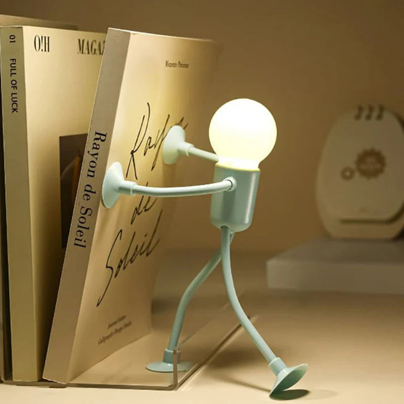Mintgrüne Figurenlampe stemmt sich mit beiden Saugnapf-Händen gegen ein Buch im Regal und leuchtet warm. 9