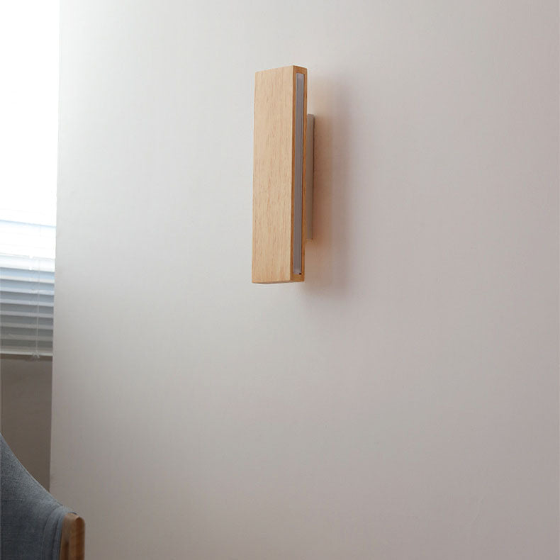 Seitenansicht der senkrecht montierten Holzleuchte, ausgeschaltet, an einer hellen Wand neben einem Fenster mit Jalousie. 2