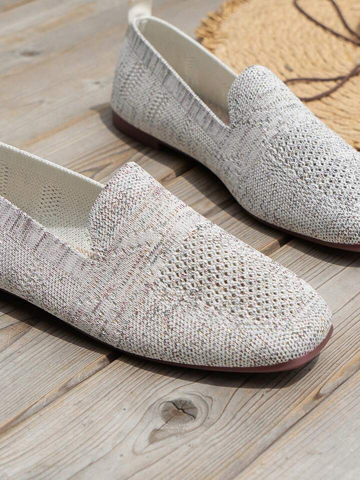 Nahaufnahme weiß-grauer melierter Slip-ons mit Lochmuster, Schlupfausschnitt und brauner Sohle auf Holzdielen. 16