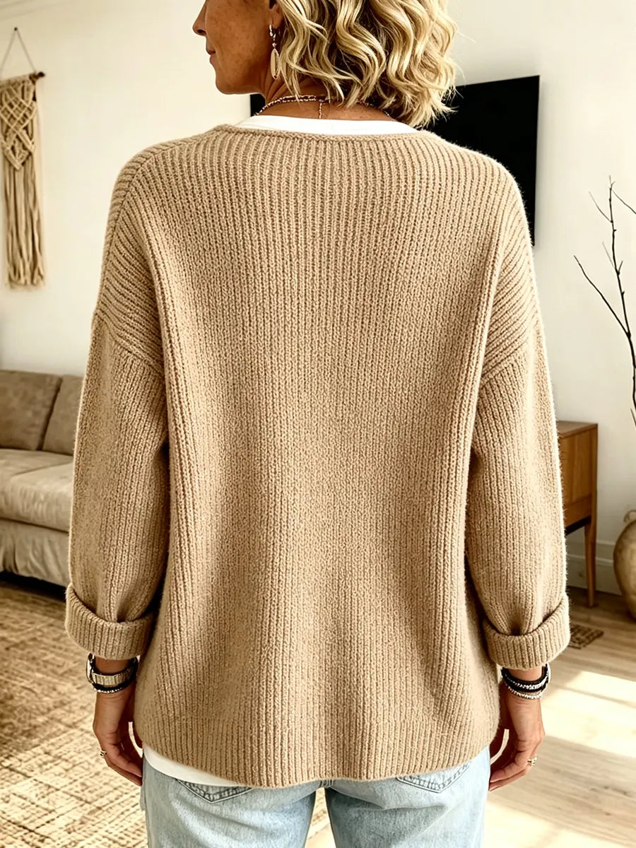 Rückansicht der beigen Strickjacke mit Rippstruktur, umgeschlagenen Ärmelbündchen und lockerem Schnitt, getragen von einer 2