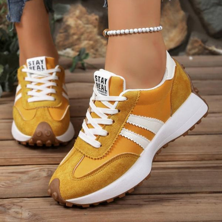 Gelbe Sneaker mit weißen Streifen und Plateausohle, getragen auf Holzboden, Seiten- und Frontansicht 6