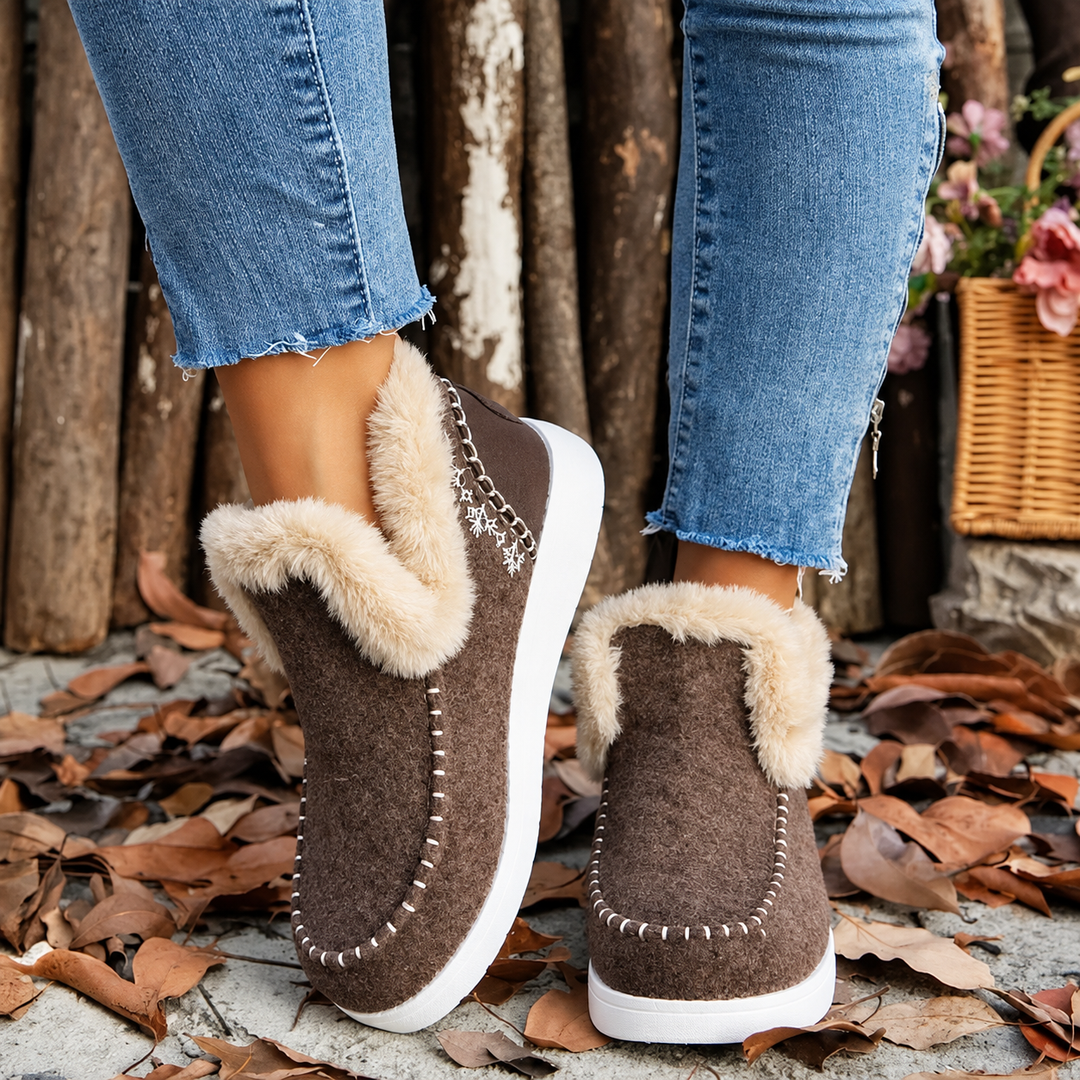 Braune Slip-On-Sneaker mit Plüschkragen und Schneeflocken-Stickerei, Schrägansicht von hinten an den Füßen zwischen Herbstblättern. 2