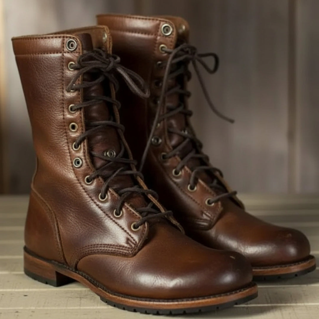 Paar hohe braune Lederstiefel mit dunklen Schnürsenkeln und Metallösen, schräg von vorn auf einem hellen Holzboden fotografiert. 1
