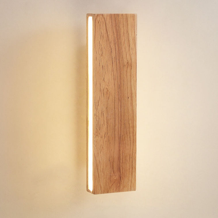Nahaufnahme der senkrechten Holzleuchte mit sichtbarer Holzmaserung und leuchtendem Streifen an der Seite vor warmem Wandlicht. 14