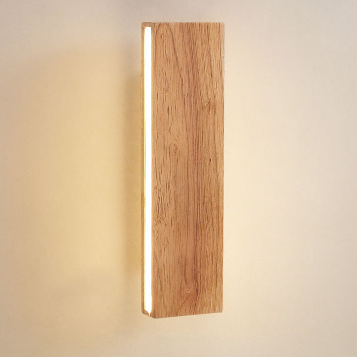 Nahaufnahme der senkrechten Holzleuchte mit sichtbarer Holzmaserung und leuchtendem Streifen an der Seite vor warmem Wandlicht. 14