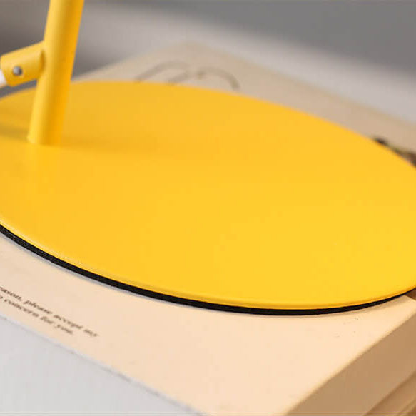 Nahaufnahme des runden gelben Metallfußes der Lampe, der auf einem Buch steht, mit dunklem Rand an der Unterseite. 4