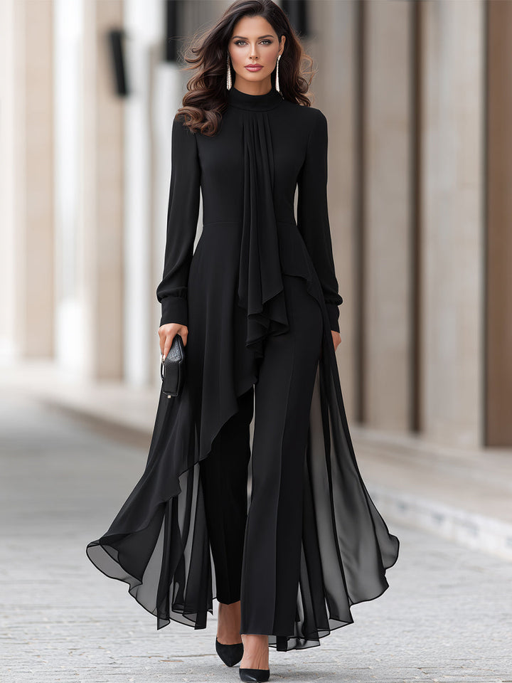 Ganzkörperansicht einer Frau in schwarzem Chiffon-Set aus Tunika mit drapiertem Halstuch und weiter Hose, dazu schwarze Pumps und Clutch. 2