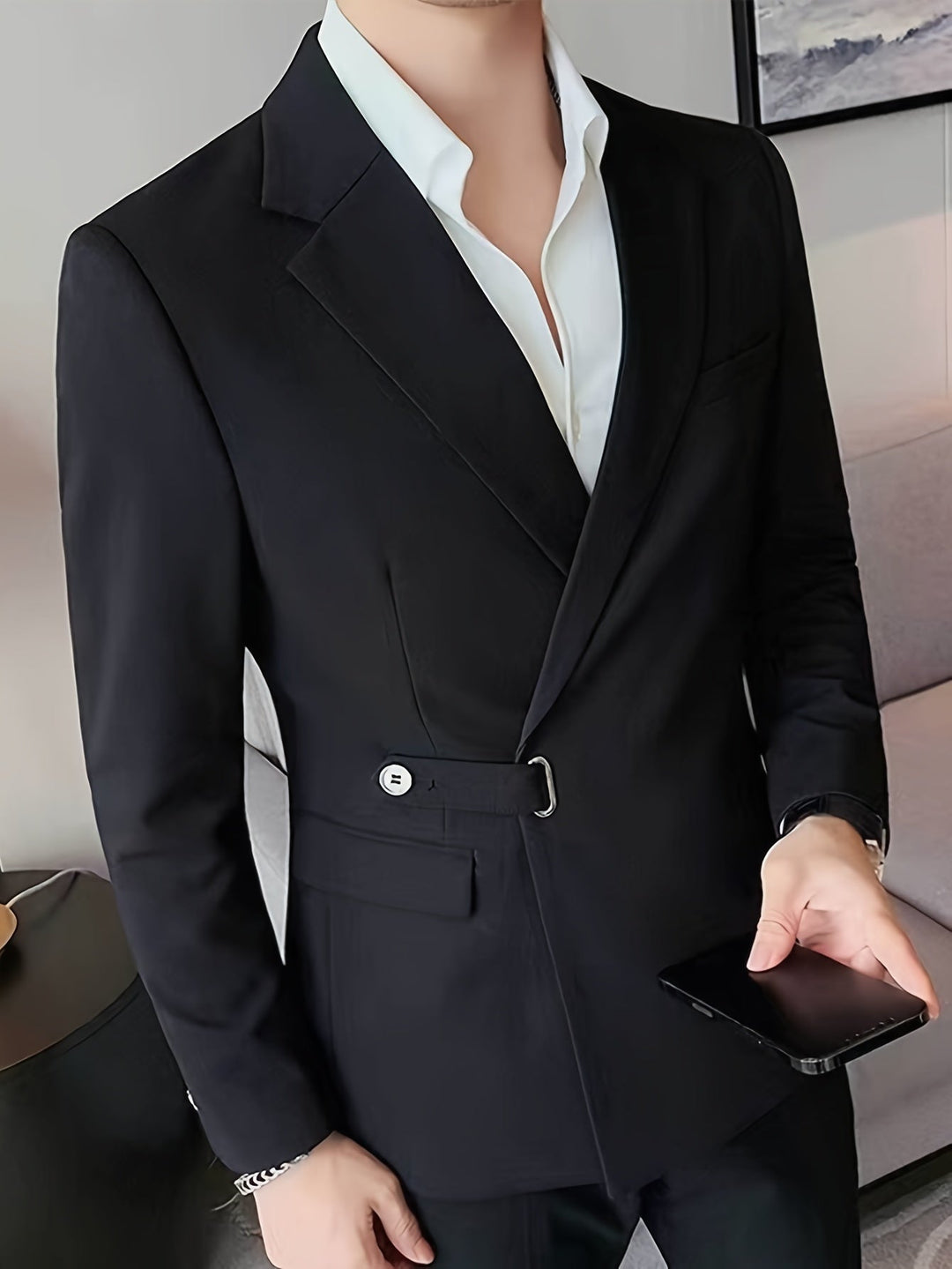 Mann im eleganten schwarzen Anzug mit weißem Hemd, hält Smartphone, modernes Wohnzimmer.