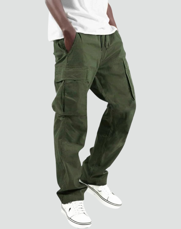 Model trägt die olivgrüne Cargohose mit Seitentaschen und Kordelzug zu weißem T-Shirt und weißen Sneakern, Seitenansicht vor grauem Hintergrund. 1