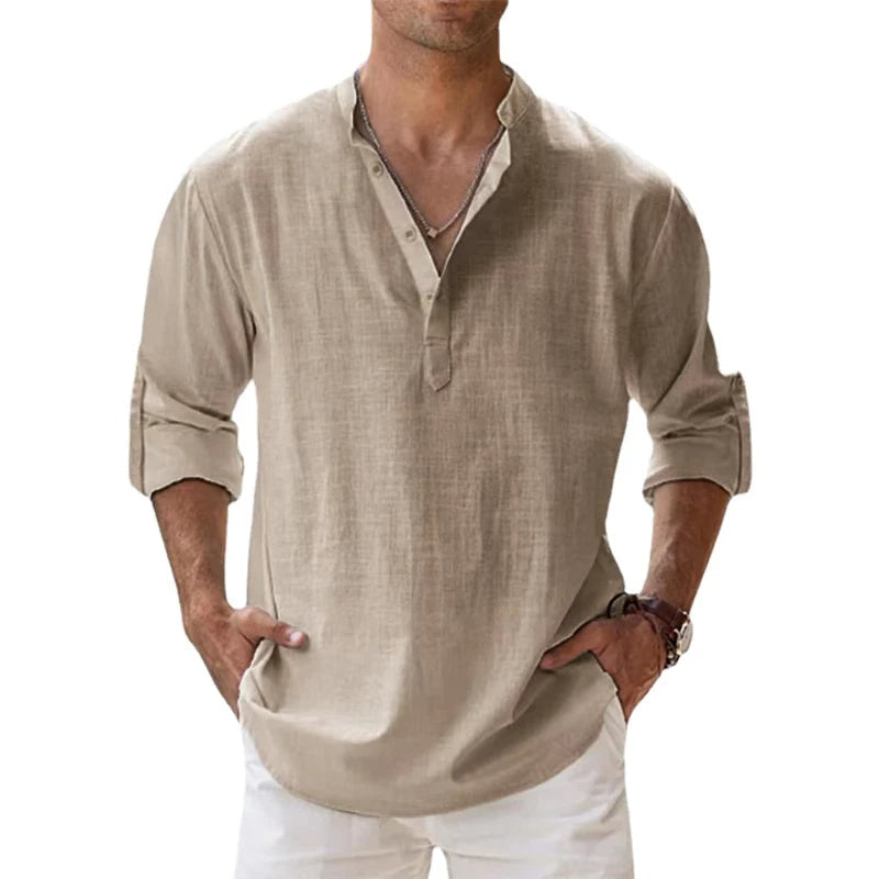 Mann trägt das lockere Henley-Shirt in Beige mit hochgekrempelten Ärmeln, Hände in den Hosentaschen, dazu weiße Hose. 1