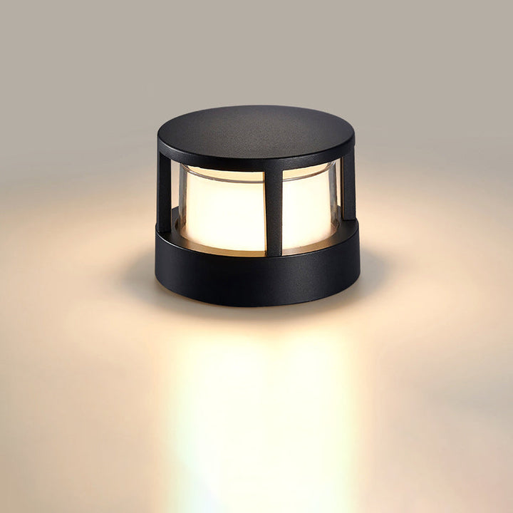 Runde schwarze Leuchte mit geschlossenem Deckel und leuchtendem Milchglas-Zylinder vor neutralem Hintergrund, warmes Licht auf dem Boden. 8