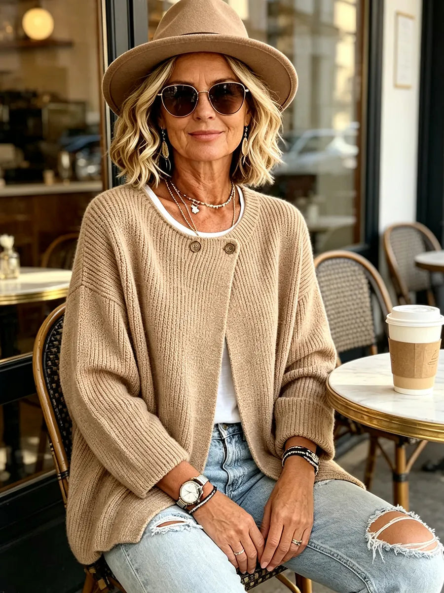 Frau mit Hut und Sonnenbrille trägt die beige Strickjacke an einem Café-Tisch im Freien 5