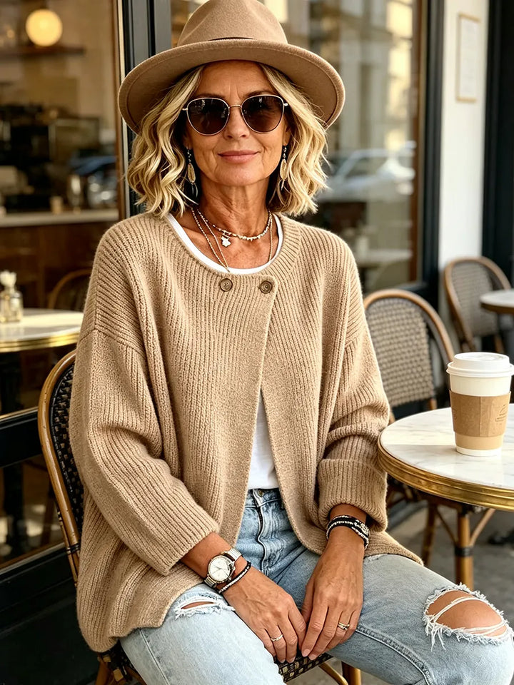 Frau mit Hut und Sonnenbrille trägt die beige Strickjacke an einem Café-Tisch im Freien 5
