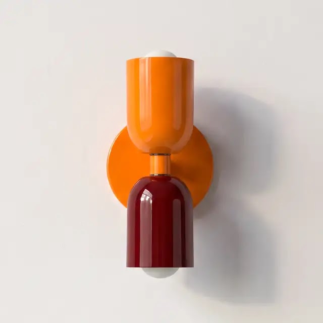 Wandlampe mit orangem oberem Schirm, orangefarbener Wandplatte und dunkelrotem unterem Schirm vor heller Wand. 25