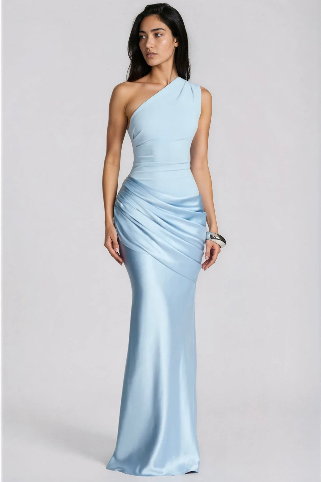Frau im hellblauen One-Shoulder-Maxikleid mit glänzendem Satinrock und gerafftem Hüftdrapé, Blick zur Seite, mit silbernem Armreif, Ganzkörperansicht. 1