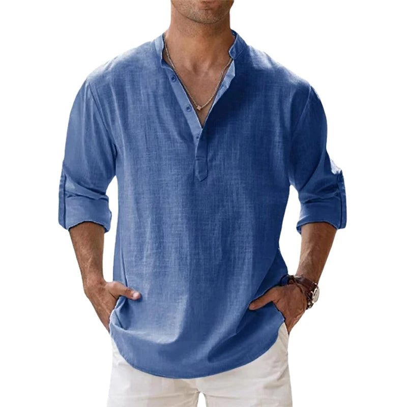 Mann trägt das lockere Henley-Shirt in Blau mit kurzer Knopfleiste und hochgekrempelten Ärmeln, dazu weiße Hose. 2