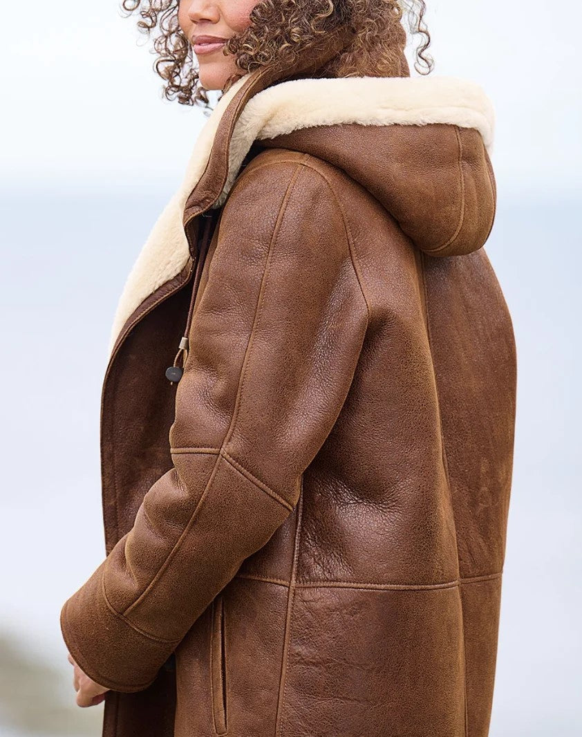 Seitenansicht des Mantels an einer Frau, mit Kapuze, weichem hellem Futter am Kragen, Ziernähten und einer Seitentasche. 2