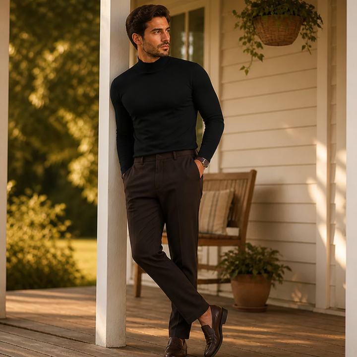 Model im schwarzen Langarmshirt mit hohem Kragen lehnt auf einer Holzveranda lässig an einer weißen Säule, die Hände in den Taschen. 3