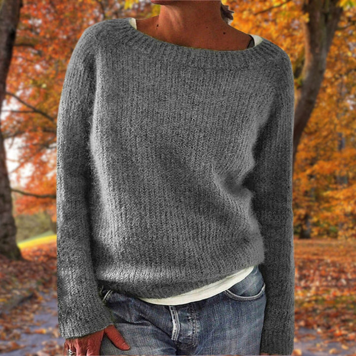 Grauer Strickpullover mit grobem Rippenstrick, von einer Frau über weißem Shirt und Jeans im Herbstwald getragen. 4