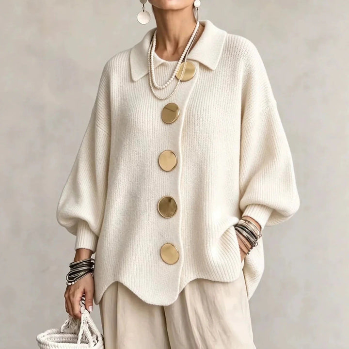 Frontansicht der Strickjacke in Creme, getragen mit Perlenketten, beiger Hose und weißer Flechttasche. 4