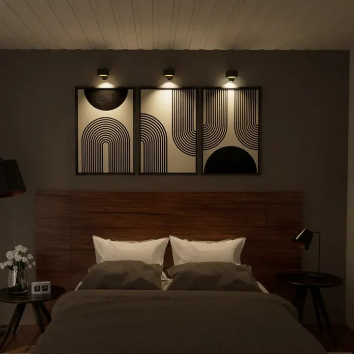 Drei schwarze Wandlampen strahlen abends drei abstrakte Bilder über einem Bett mit Holzkopfteil an. 5