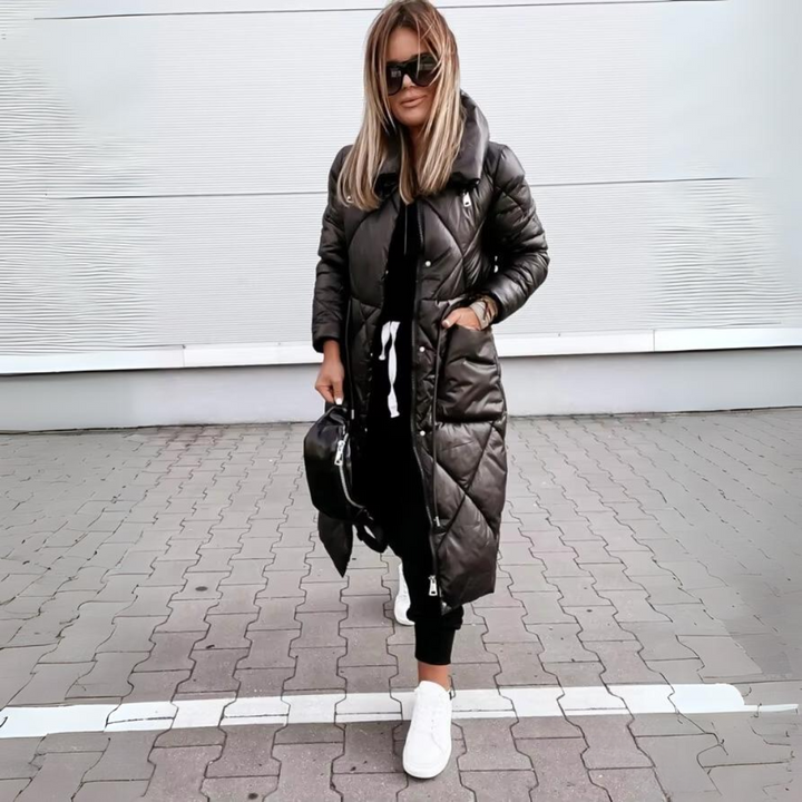 Frau mit Sonnenbrille steht auf Pflaster und trägt die lange schwarze Steppjacke geschlossen, eine Hand in der Seitentasche. 5