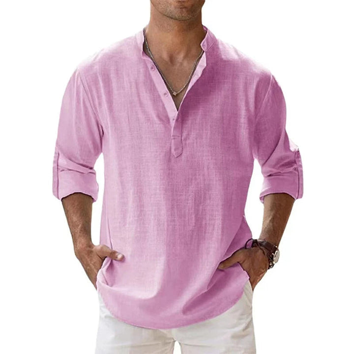 Mann trägt das lockere Henley-Shirt in Rosa mit Stehkragen und aufgerollten Ärmeln, Hände in den Hosentaschen. 3