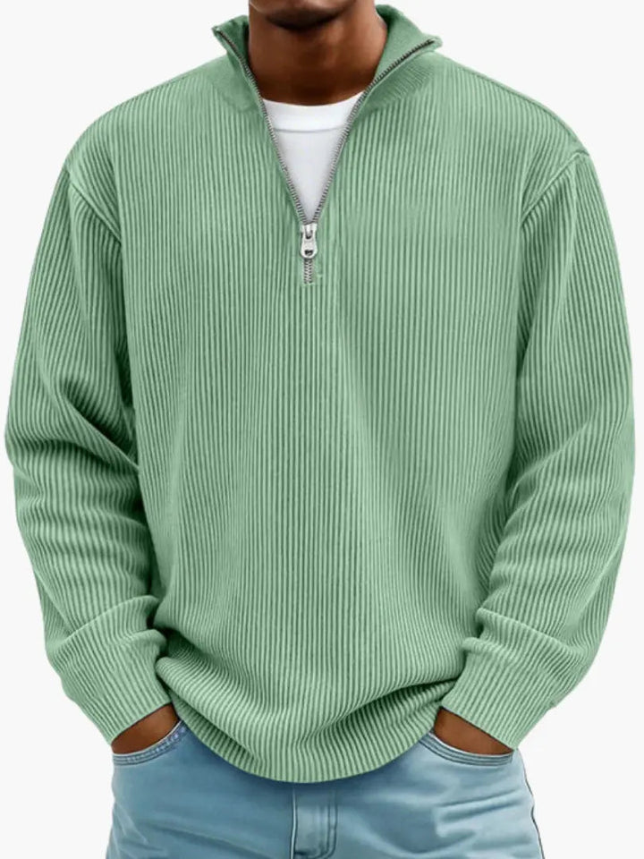 Mann trägt den gerippten Pullover in hellem Grün mit Viertelreißverschluss, Hände in den Taschen einer blauen Jeans. 3