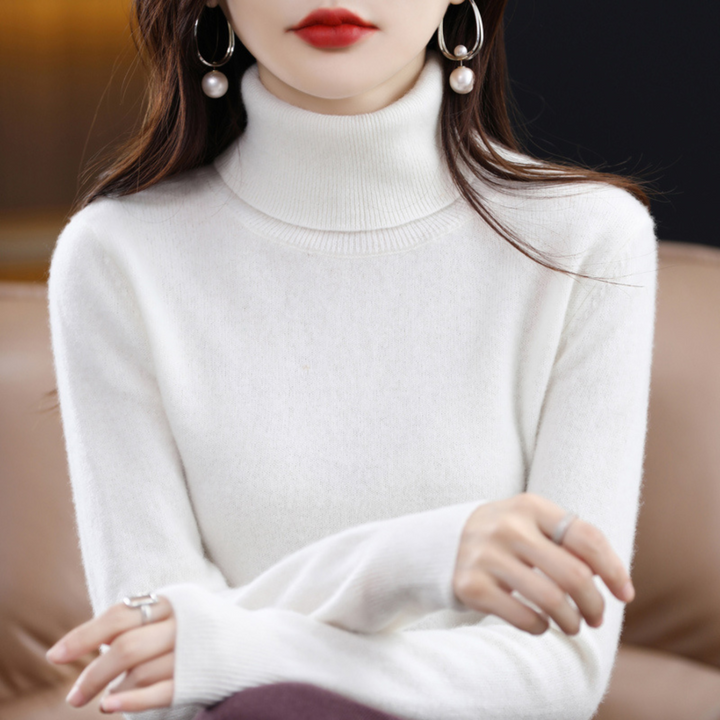 Weißer Rollkragenpullover am sitzenden Model mit verschränkten Armen, flauschige Strickoberfläche und gerippter Kragen. 12
