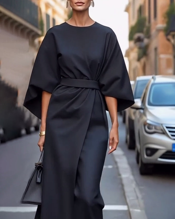 Schwarzes Wickelkleid mit weiten Ärmeln und Taillengürtel, von vorn getragen mit Ohrringen und kleiner schwarzer Tasche auf einer Straße. 6