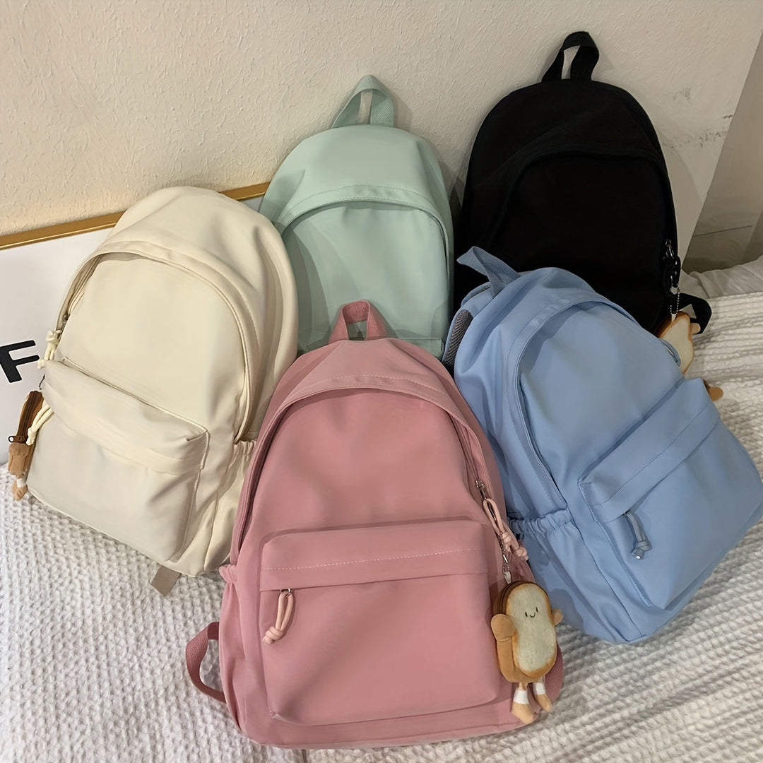 Fünf Rucksäcke in Creme, Mintgrün, Schwarz, Rosa und Hellblau liegen auf einer Decke, an zwei hängen kleine Brot-Plüschanhänger. 8