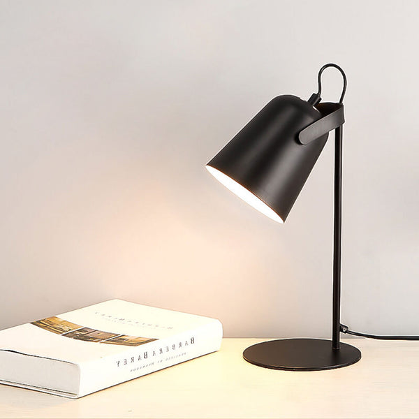 Schwarze Tischlampe mit neigbarem Schirm auf einem hellen Tisch, daneben ein aufgeschlagenes Buch vor heller Wand. 12