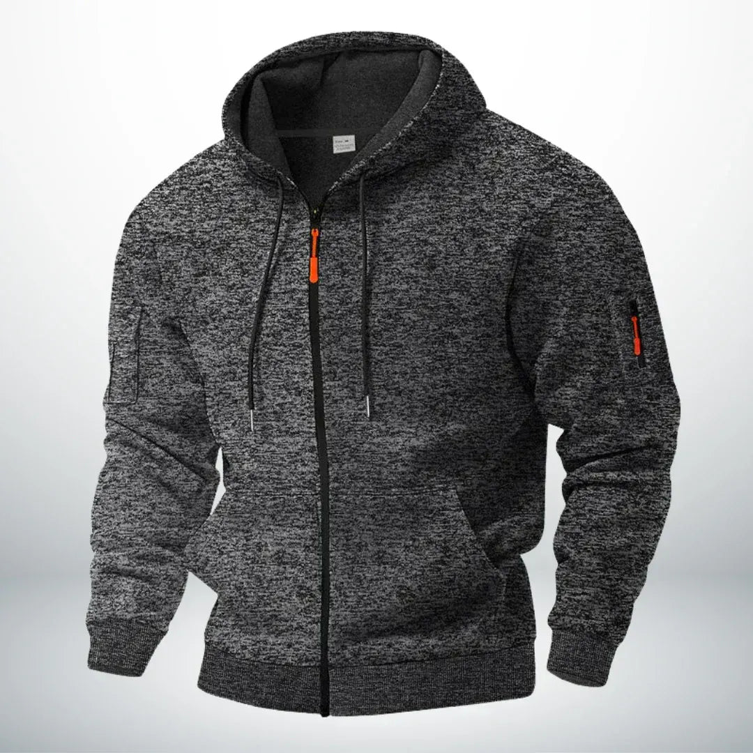 Kapuzenjacke in dunklem, meliertem Anthrazit, frontal von schräg gezeigt, mit orangefarbenem Zipper an Front und Ärmeltasche. 5