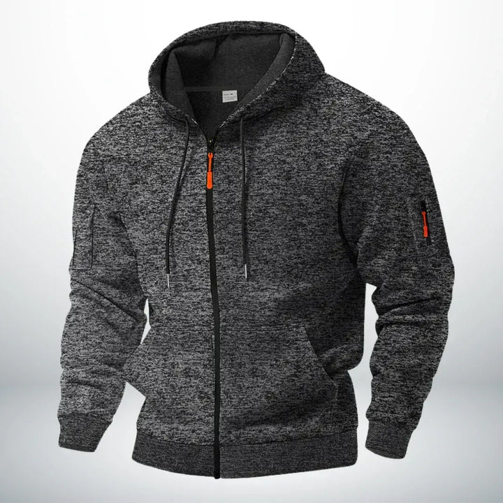 Kapuzenjacke in dunklem, meliertem Anthrazit, frontal von schräg gezeigt, mit orangefarbenem Zipper an Front und Ärmeltasche. 5