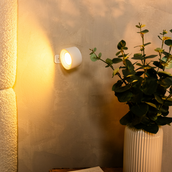 Weiße Wandlampe leuchtet seitlich zur Wand gedreht und taucht eine Wandfläche neben einer Vase mit Eukalyptus in warmes Licht. 14