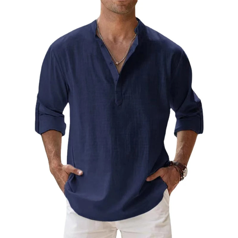 Mann trägt das lockere Henley-Shirt in dunklem Marineblau mit Stehkragen und hochgekrempelten Ärmeln, dazu weiße Hose. 5