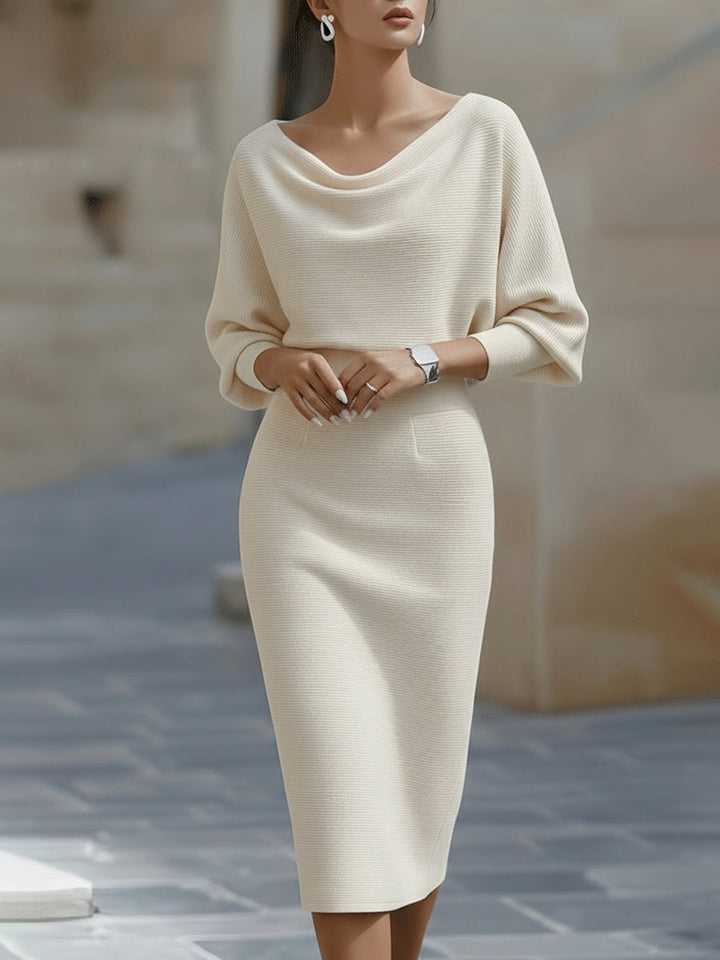 Frontansicht: Model in cremefarbenem Strickkleid mit weichem Wasserfallausschnitt, Fledermausärmeln und schmal geschnittenem Rock bis zur Wade. 3