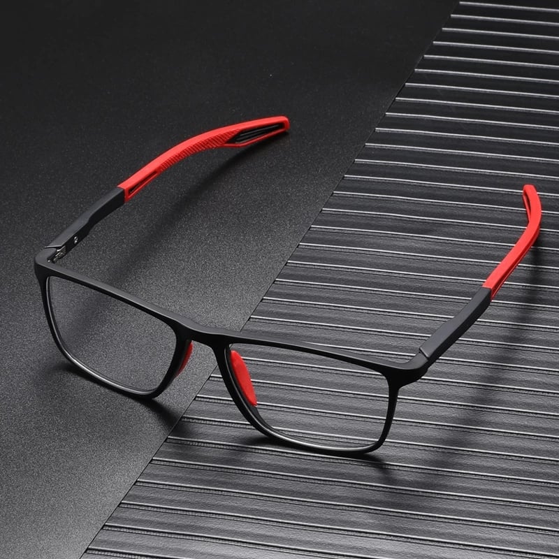 Sportbrille mit schwarzem Rahmen und roten Bügelenden, schräg auf dunklem, gerilltem Untergrund liegend. 7