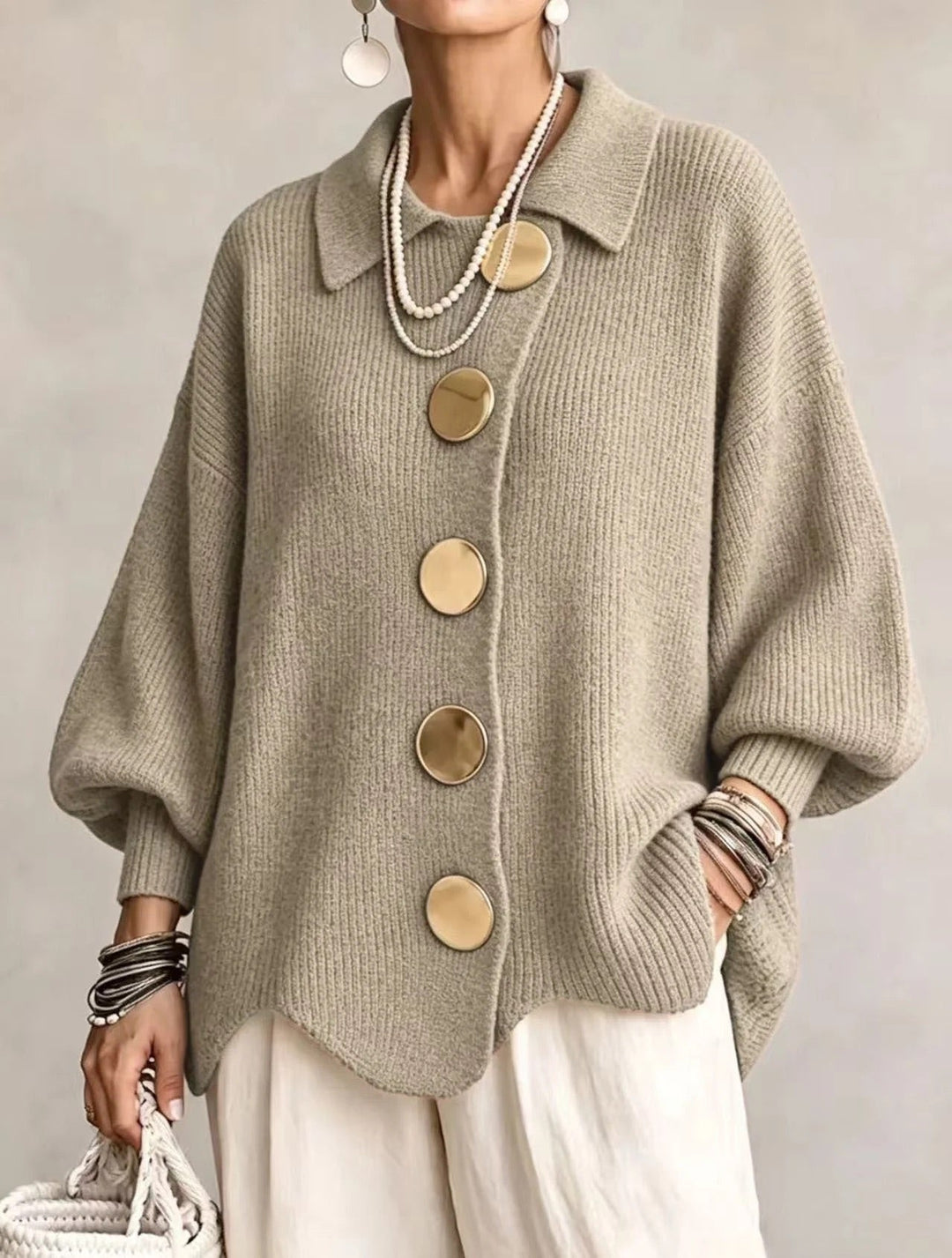 Strickjacke in gedecktem Salbeigrün-Beige mit goldfarbenen Knöpfen, getragen zu weißer Hose und Perlenketten, Frontansicht. 17