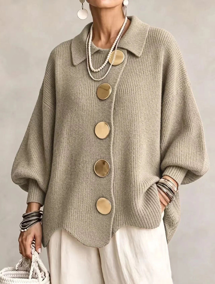 Strickjacke in gedecktem Salbeigrün-Beige mit goldfarbenen Knöpfen, getragen zu weißer Hose und Perlenketten, Frontansicht. 17