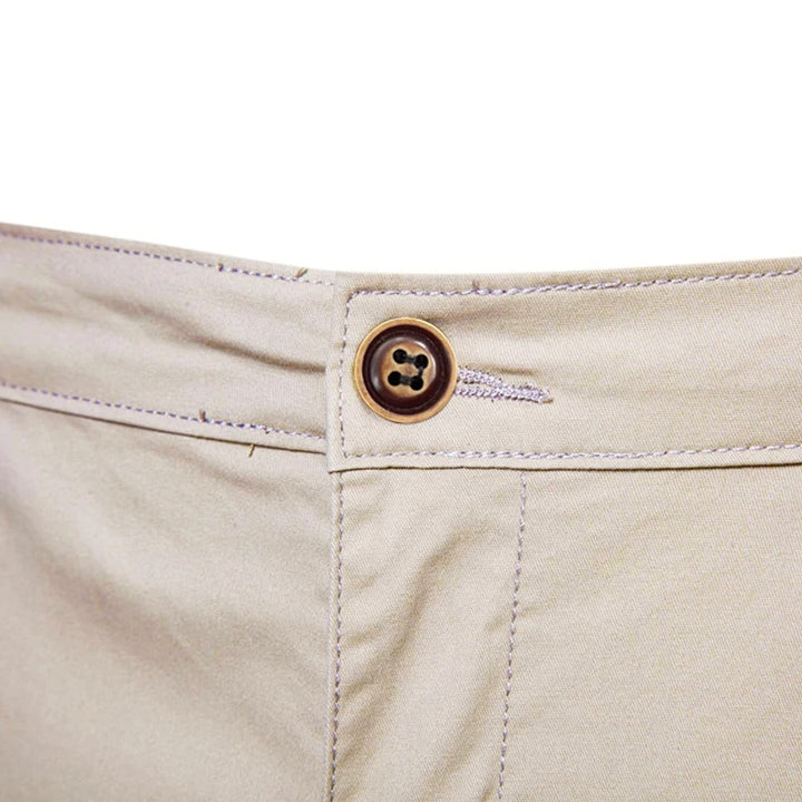 Nahaufnahme des braunen Knopfs mit Knopfloch am Bund der beigen Shorts, umgeben von hellen Steppnähten. 5