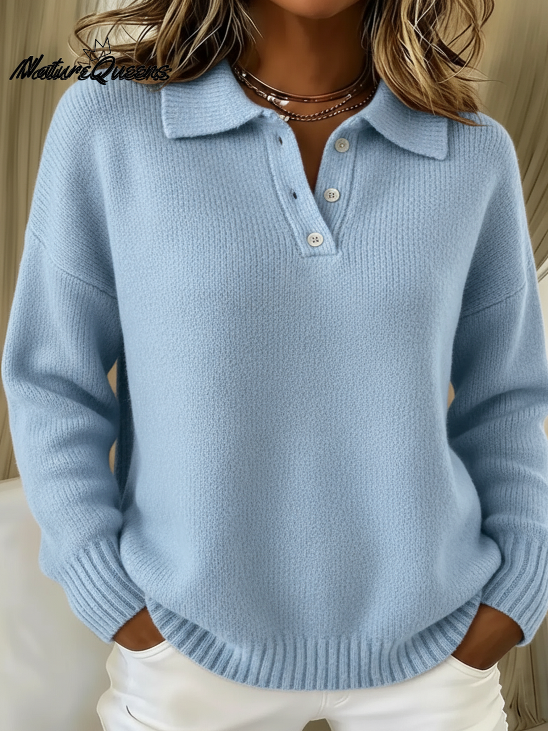 Frau trägt den Strickpullover in Hellblau, Vorderansicht mit Polokragen, Knopfleiste und gerippten Bündchen, die Hände in den Hosentaschen. 1