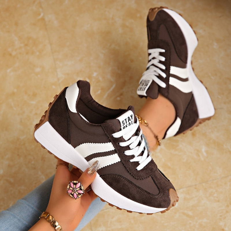 Braune Sneaker mit weißen Streifen, in der Hand gehalten, daneben ein getragener Schuh auf Marmorboden 3