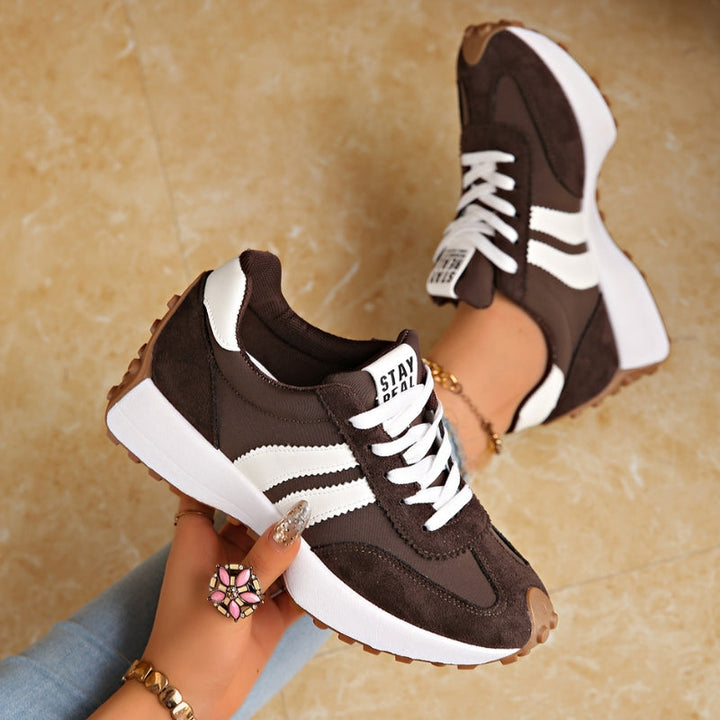 Braune Sneaker mit weißen Streifen, in der Hand gehalten, daneben ein getragener Schuh auf Marmorboden 3