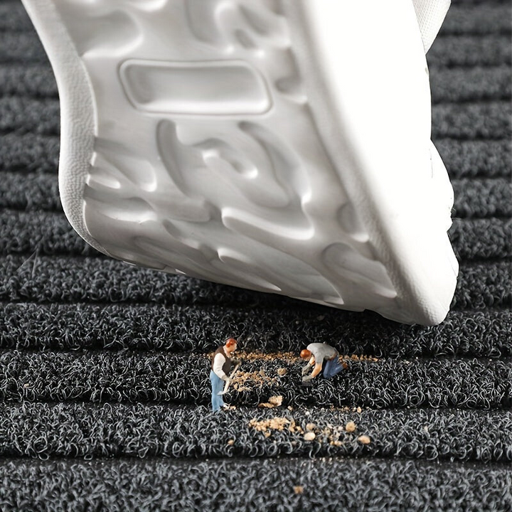 Detailansicht der Schlingenoberfläche mit einer Schuhsohle darüber und Miniaturfiguren, die Schmutzkrümel zusammenkehren. 4